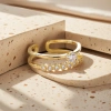 The golden double-layered ring features multiple round transparent gemstones on the upper layer and a large round transparent gemstone in the center on the lower layer. It has a white stone countertop Specification image